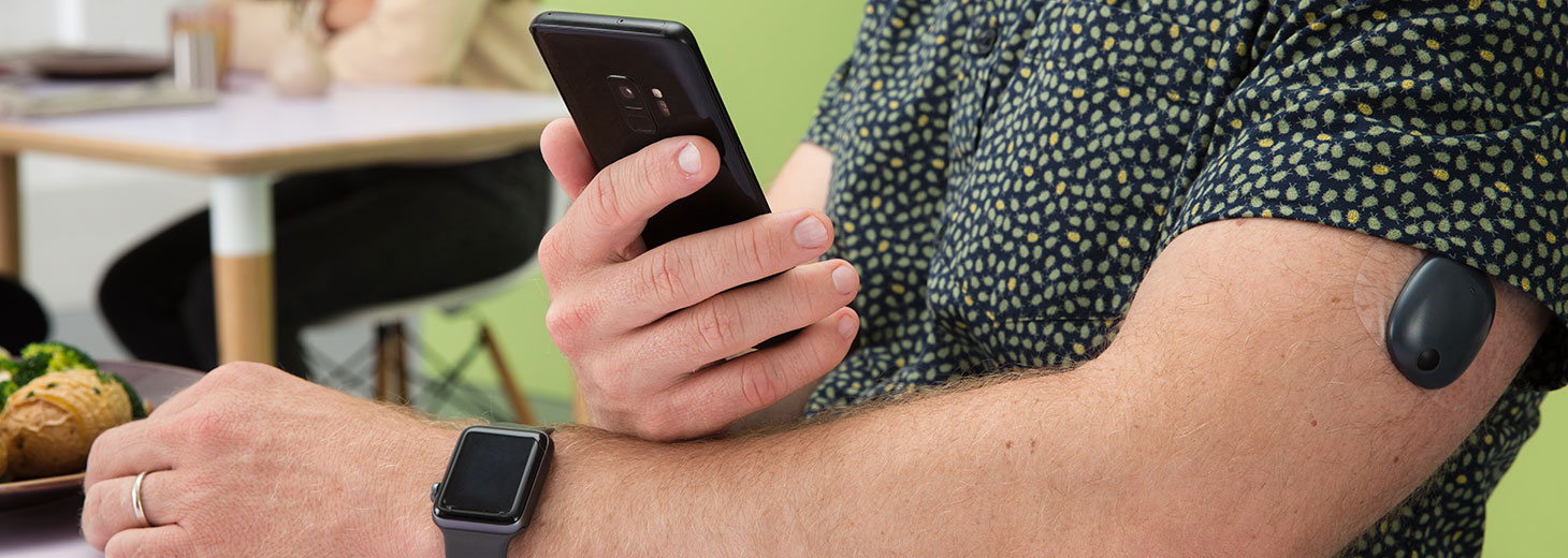 Ricky, living with Type 1 diabetes, checking his phone with his sensor on his arm