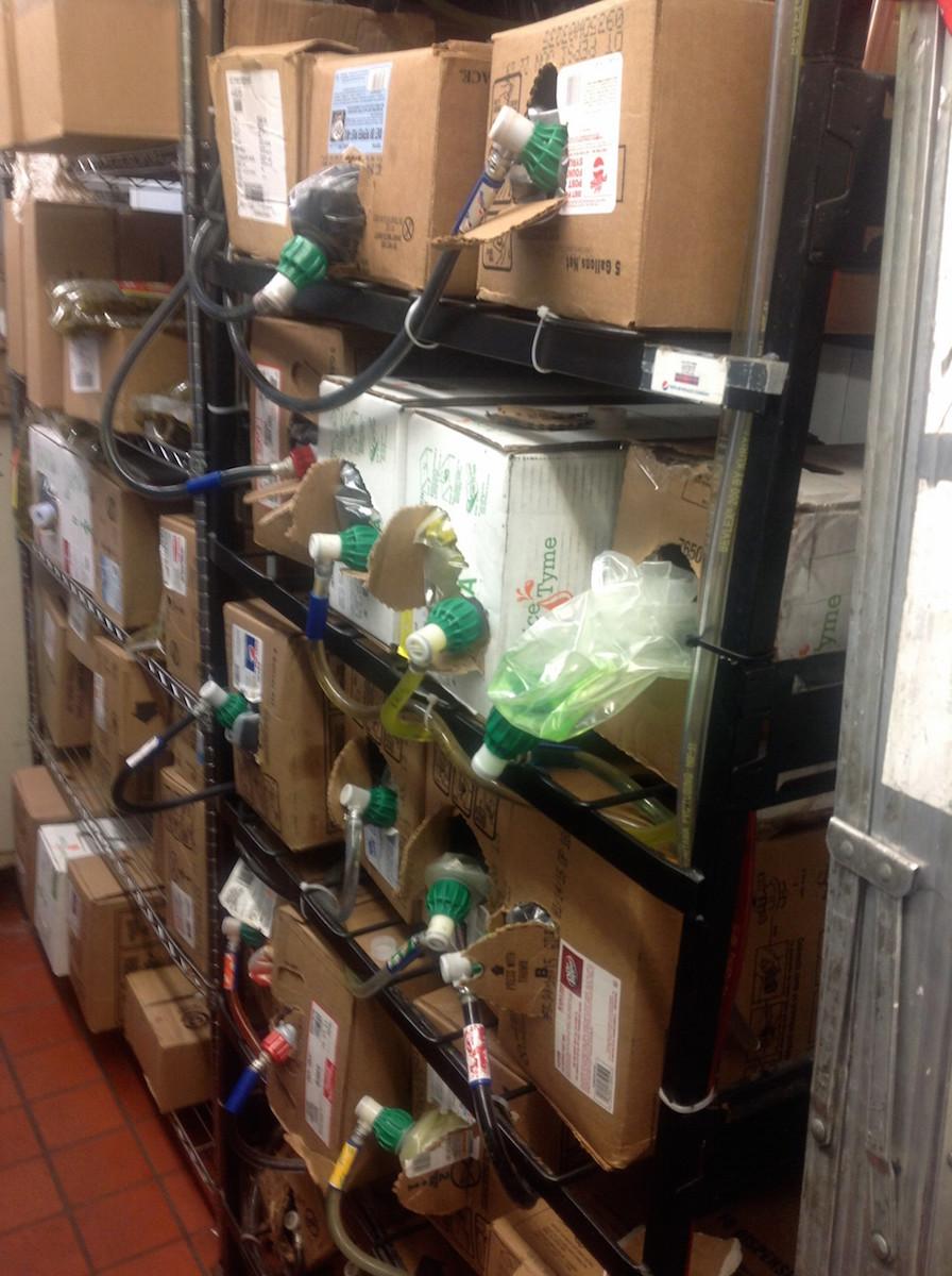 Drink station shelving with boxes of post mix flavor syrup